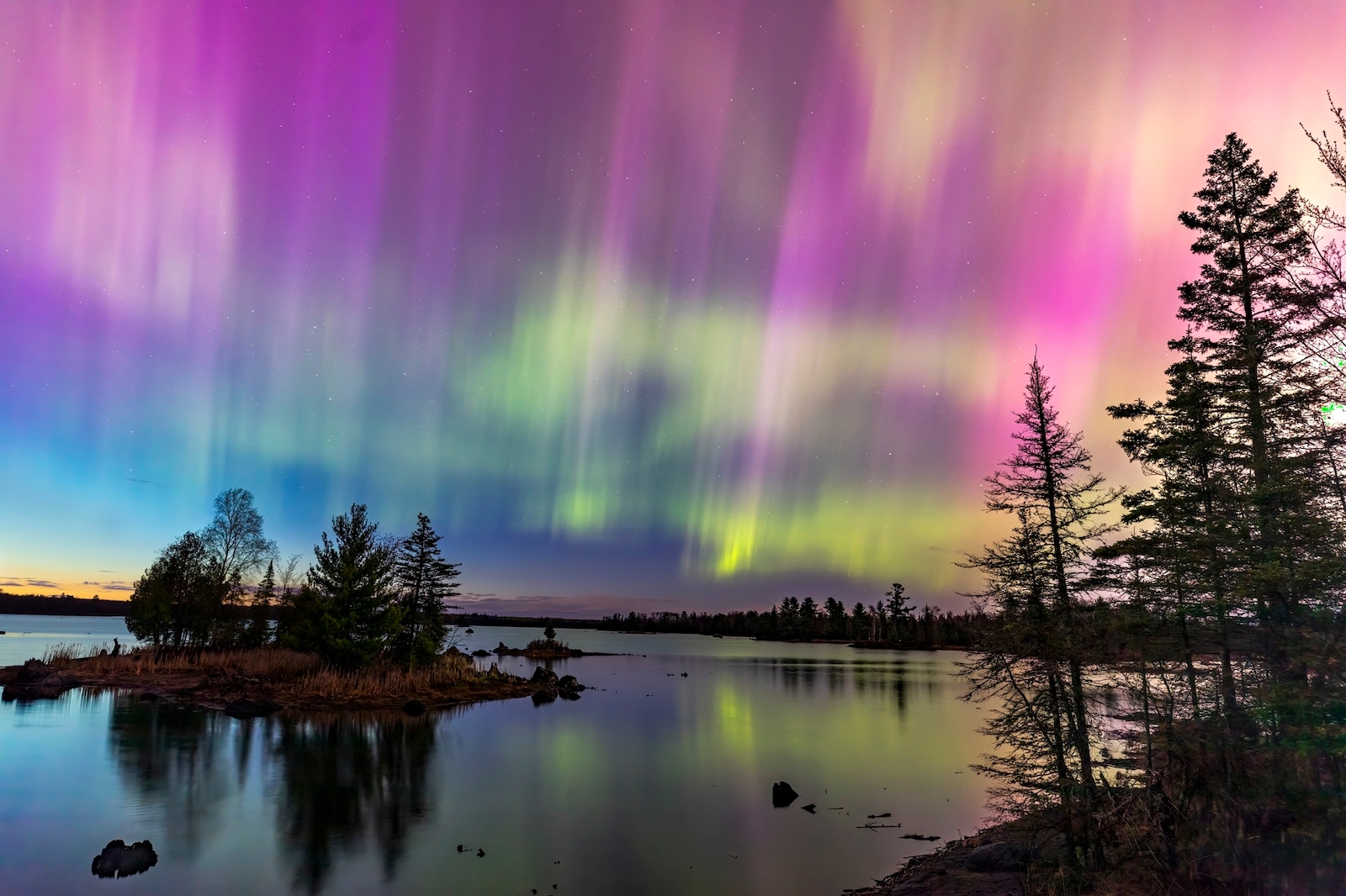 The aurora borealis illuminates the night sky above a tranquil lake, creating a stunning display of colors and reflections