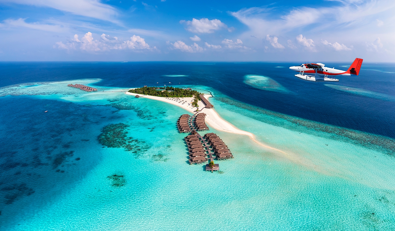 Aerial view of a small island in the Maldives, with a small plane flying above the turquoise waters