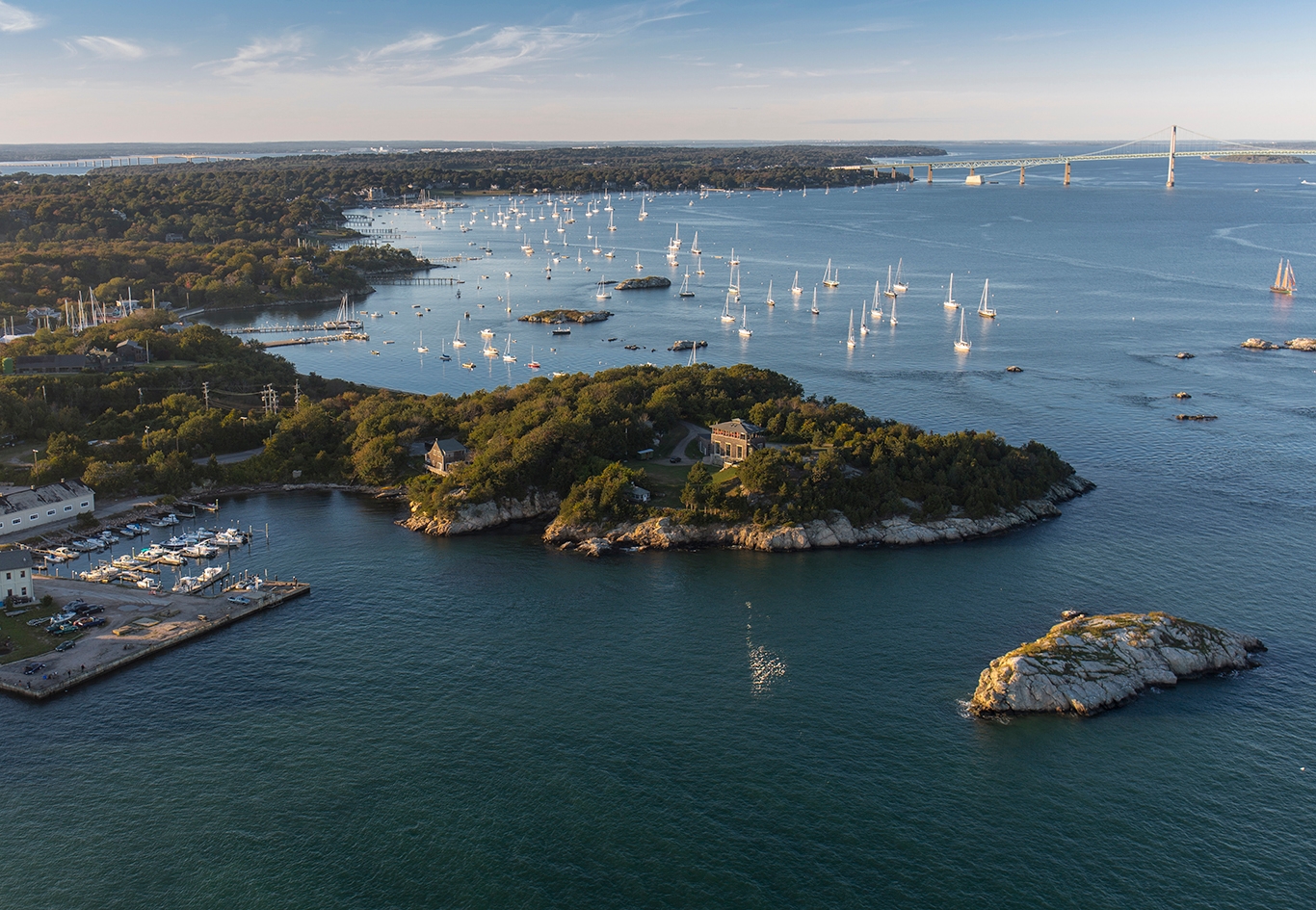A serene body of water in Newport, Rhode Island, reflecting the clear blue sky and surrounding greenery.
