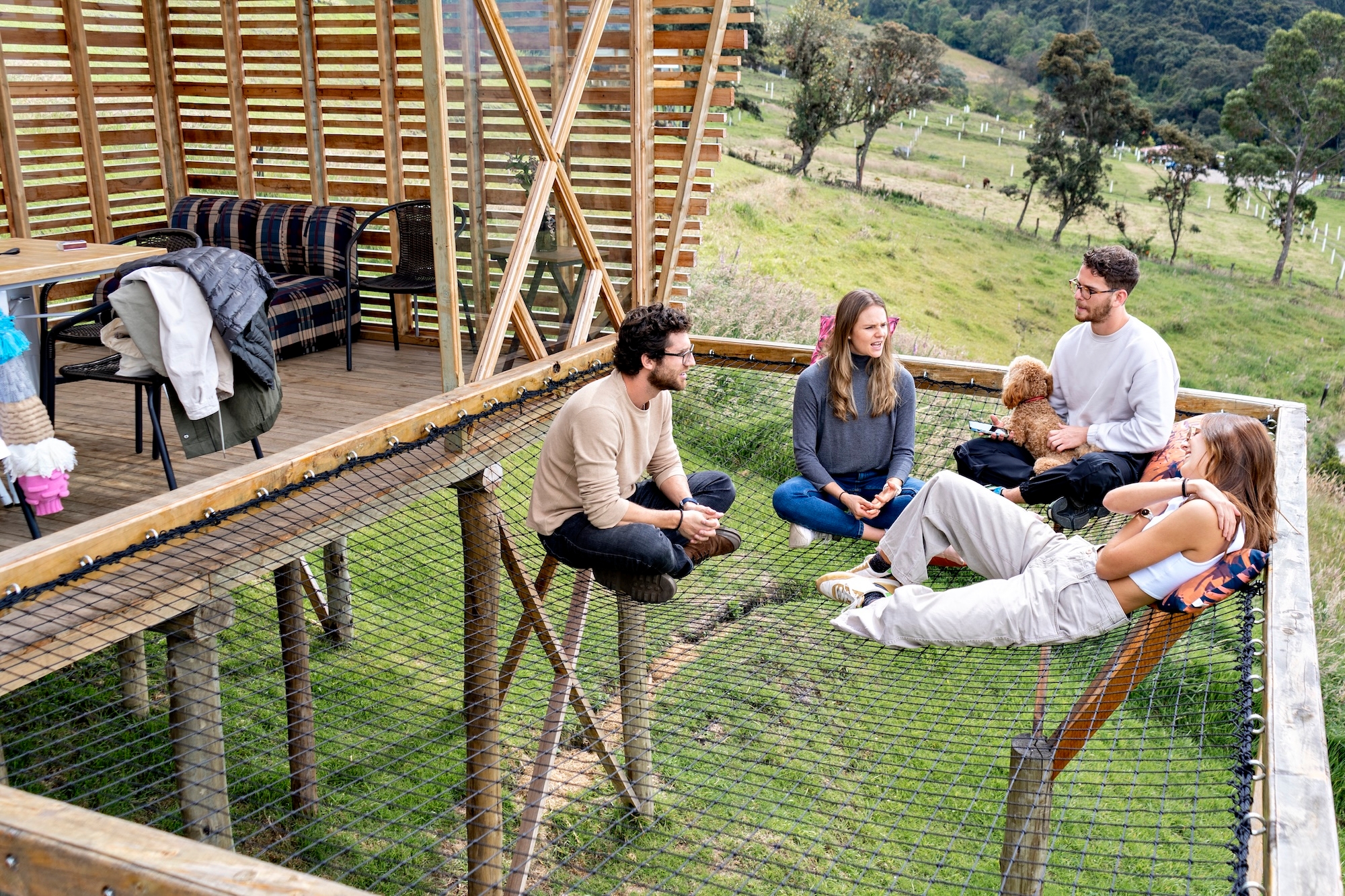 A group of 4 & a dog relax on netting in Colombian treehouse