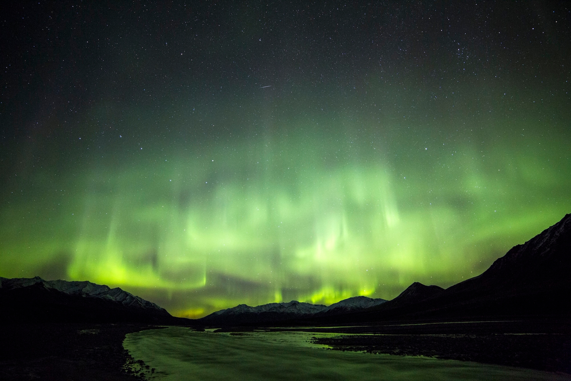 The Northern Lights offer a greenish hue above mountains