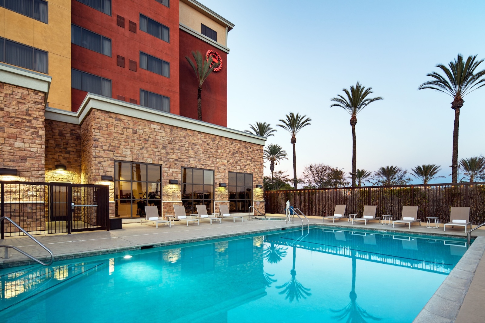 Hotel pool at Sheraton Garden Grove-Anaheim South, featuring lounge chairs and a hotel in the background