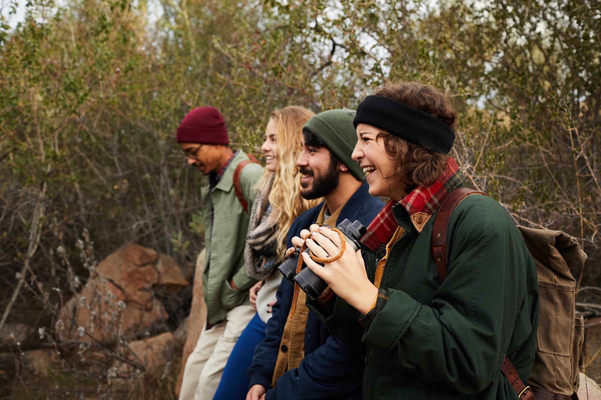 Friends laugh in nature, one scanning with binoculars