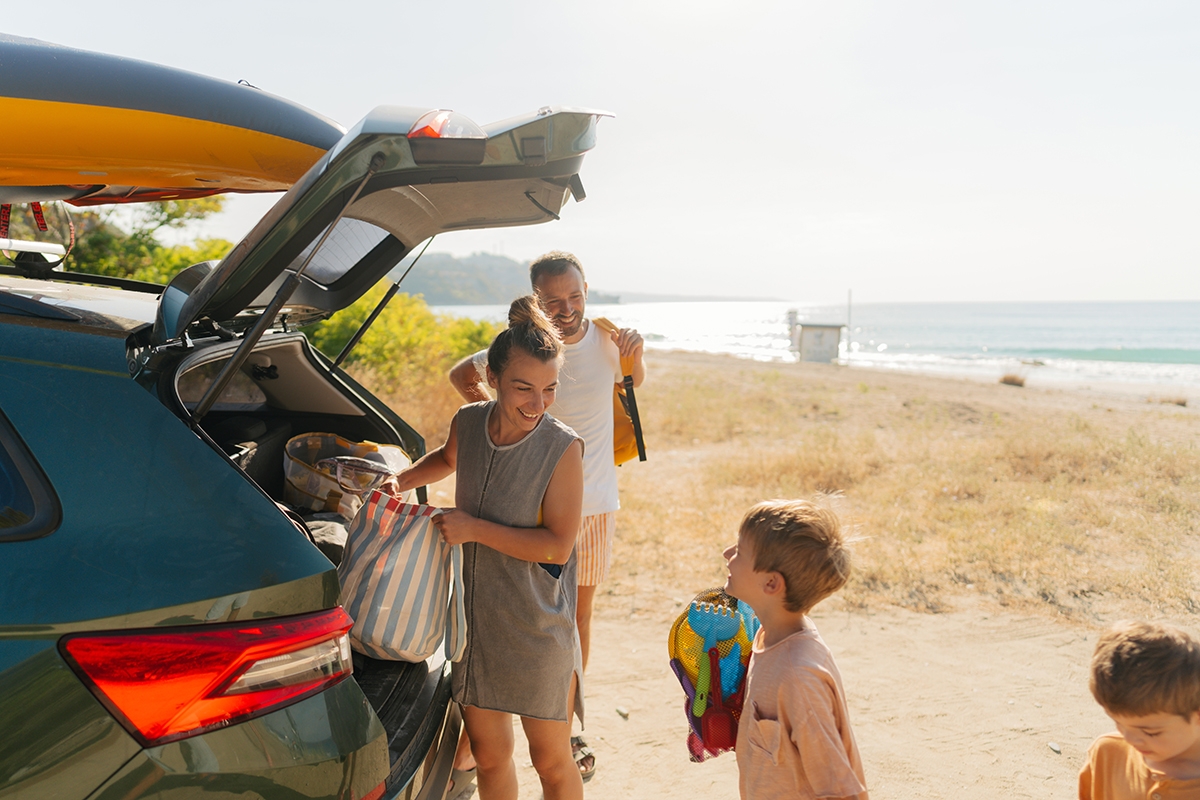  A family of four happily packing their car for a trip, with bags and gear ready to go. Reserve rental cars if needed.