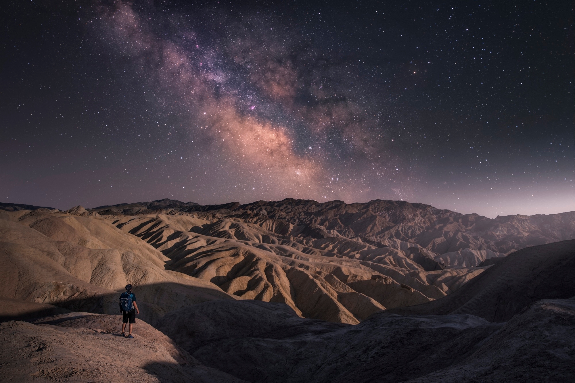 A man stands on a hill, gazing at the stars