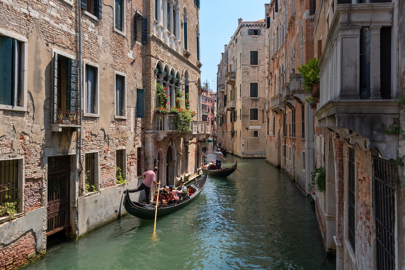A gondola glides through a narrow canal in San Marco, surrounded by historic buildings and serene water reflections