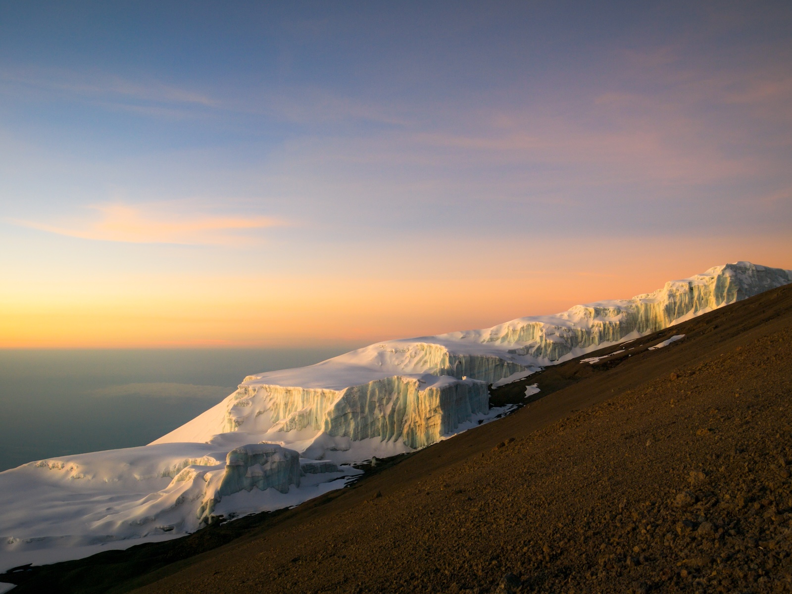 2010年、アフリカ、タンザニアのキリマンジャロ山頂の氷河。茶色の火山砂の中で孤立し、形成された印象的な氷河。空が金色とピンク色に染まった、夜明けに撮影された写真