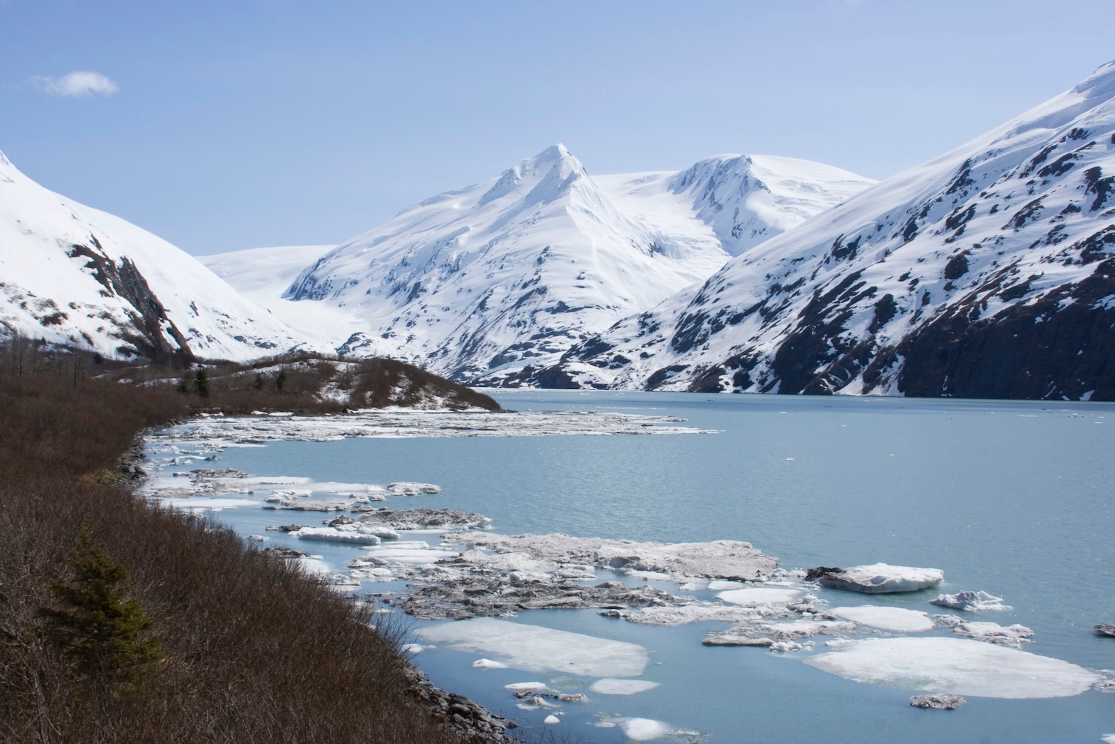 A serene lake nestled among snow-capped mountains in North Pole, Alaska, reflecting the clear blue sky