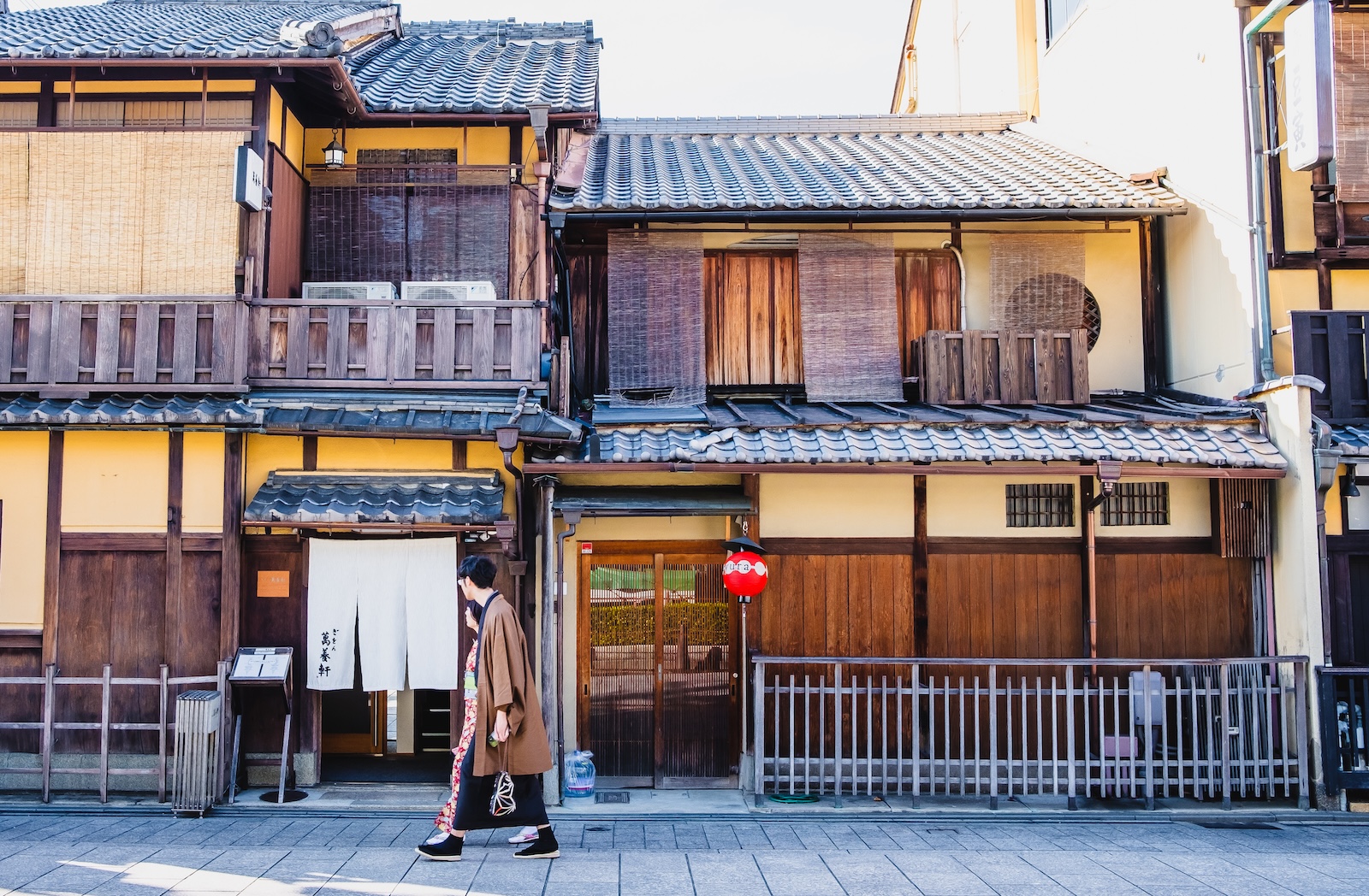 A person walks past a building with wooden shutters in Gion, showcasing traditional architecture and local culture