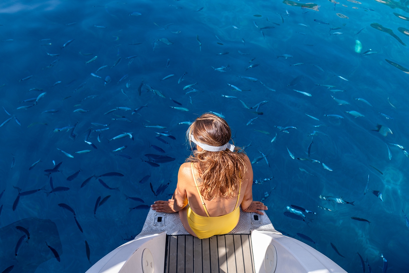 A woman in a yellow swimsuit sits on a boat with fish below