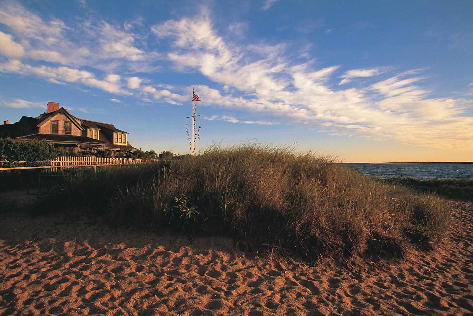 A beach house in Nantucket, Massachusetts, featuring a flag atop its roof, overlooking the ocean waves.