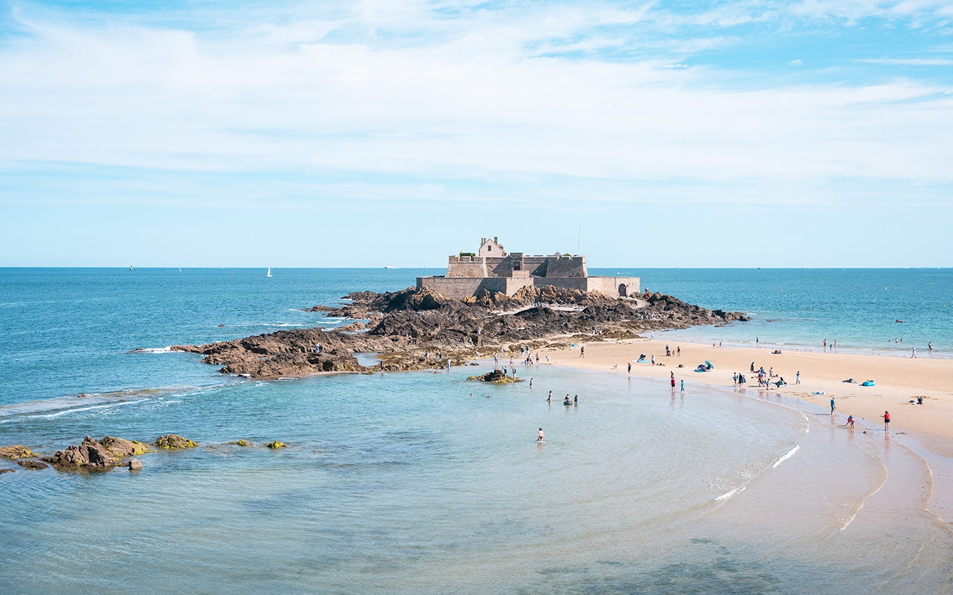 A beach in Saint-Malo, Brittany, France, featuring people enjoying the sun with a castle in the background