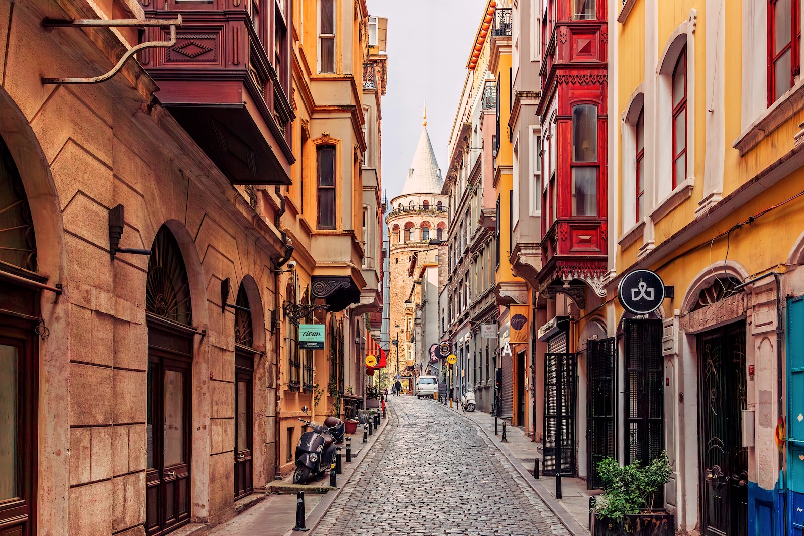 A narrow street lined with colourful buildings, featuring the iconic Galata Tower in the background.