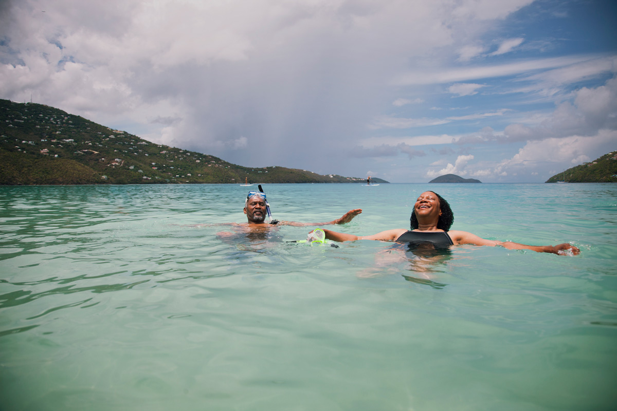 A couple joyfully floating in the ocean, arms outstretched, enjoying a sunny day together.