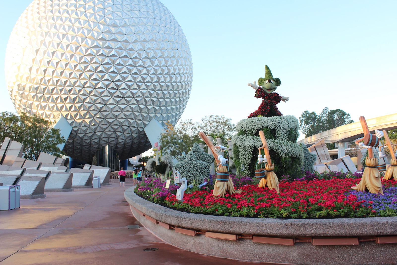 A flower bed with vibrant blooms and a flower statue of Mickey Mouse in front of the iconic dome at EPCOT, Disney World.