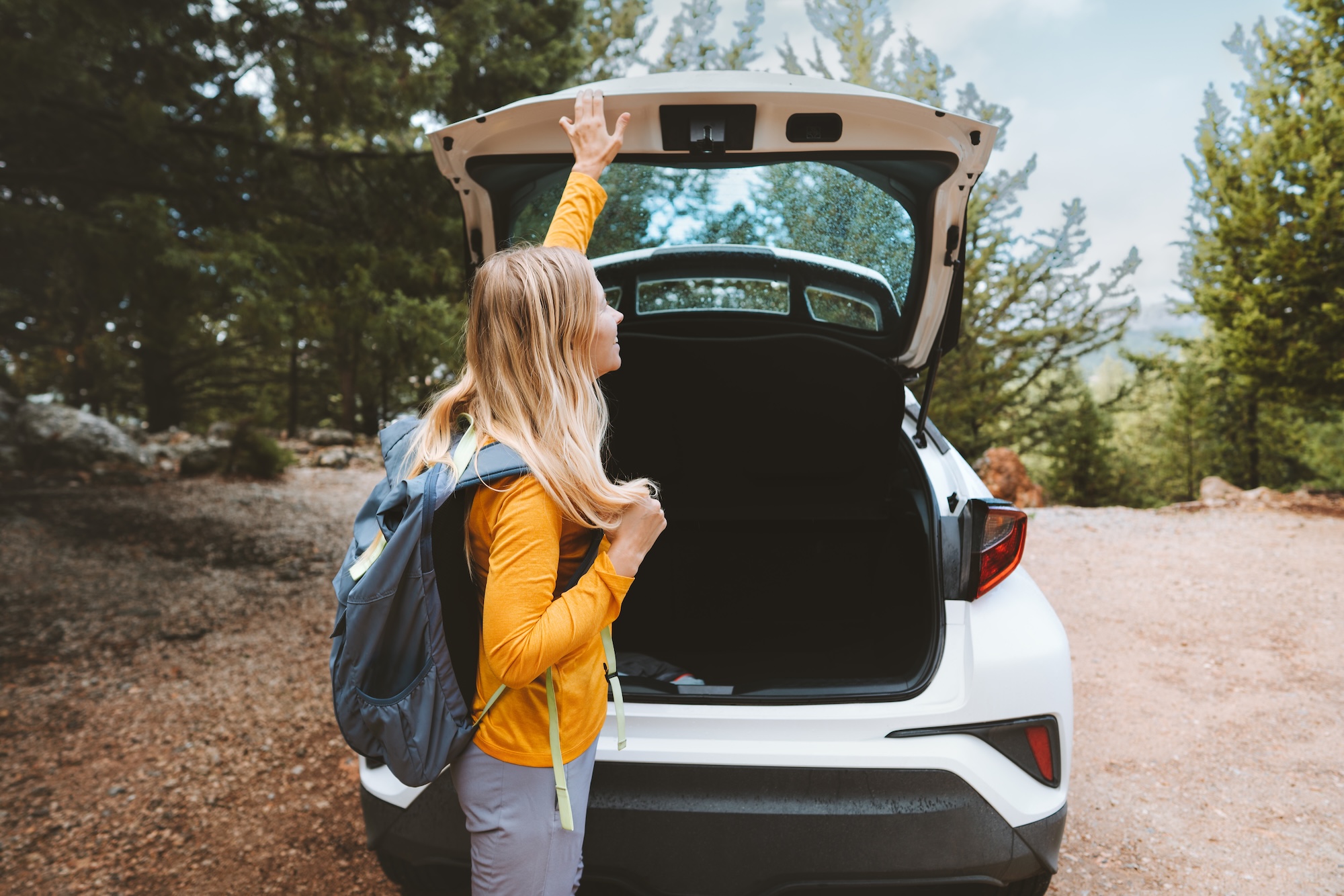 A woman in a yellow top opens the trunk of her car