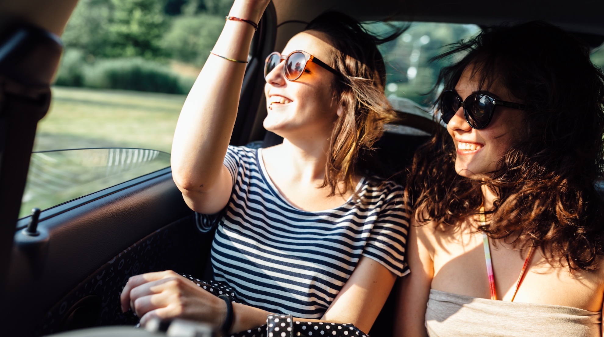 Two young women sit in a car, excited for a NYC road trip