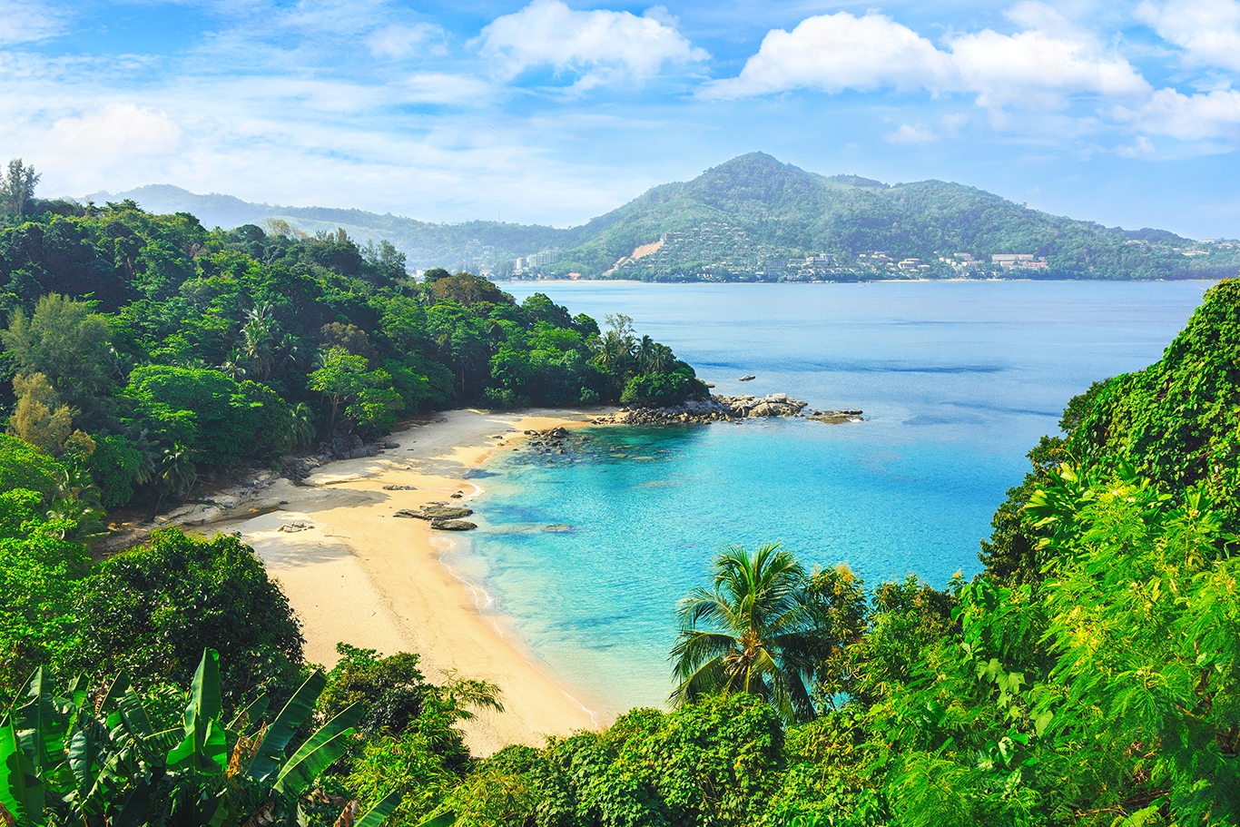A stunning beach in Phuket, Thailand, featuring a tropical forest and crystal-clear blue waters