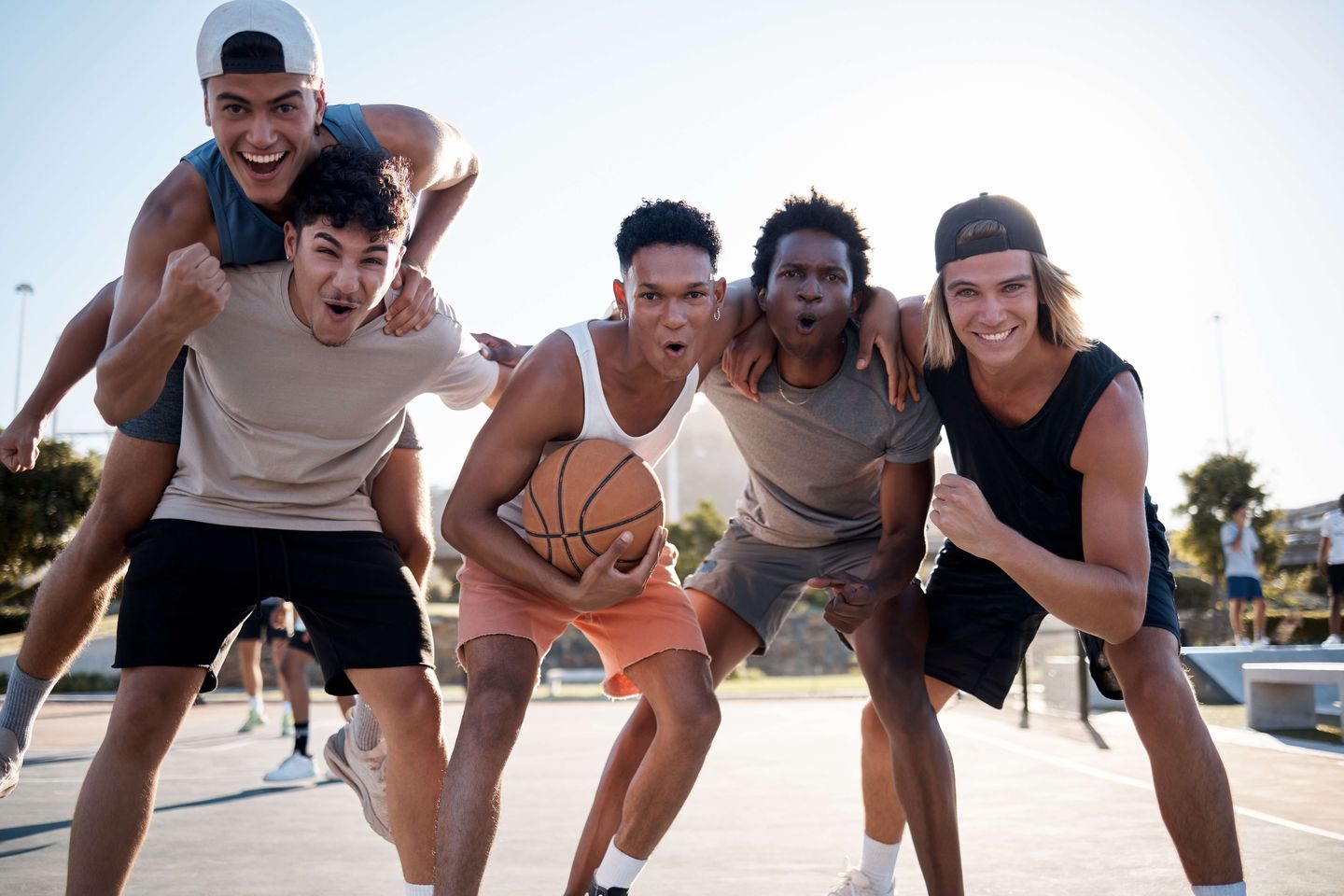 ragazzi vestiti in abiti sportivi esultano e sorridono in un campo da pallacanestro guardando in camera