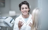 A female dentist in a white coat talking with a patient in a dental office setting.