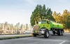 A large green truck with a GFL logo drives alongside a harbor.