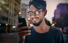 A smiling man looks at a smart phone with a city in the background.