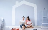 A man and a woman sit in a freshly-painted room with the outline of a house on the wall behind them.