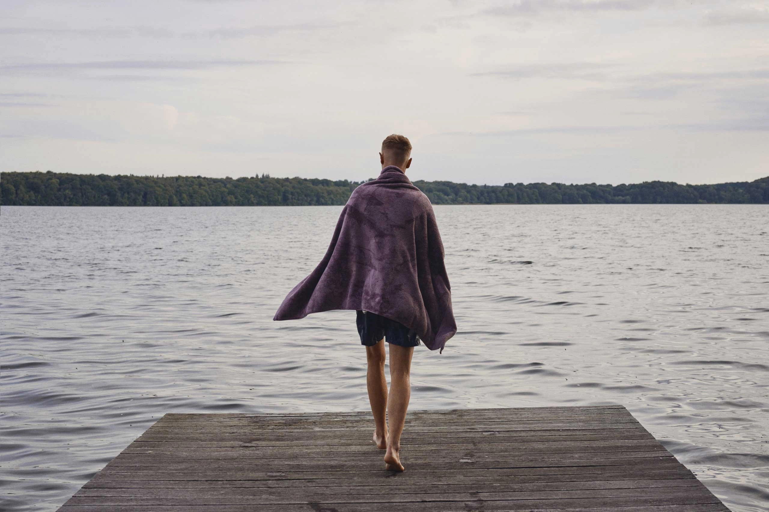 En mand står med et håndklæde om sig på en badebro og kigger ud over vandet