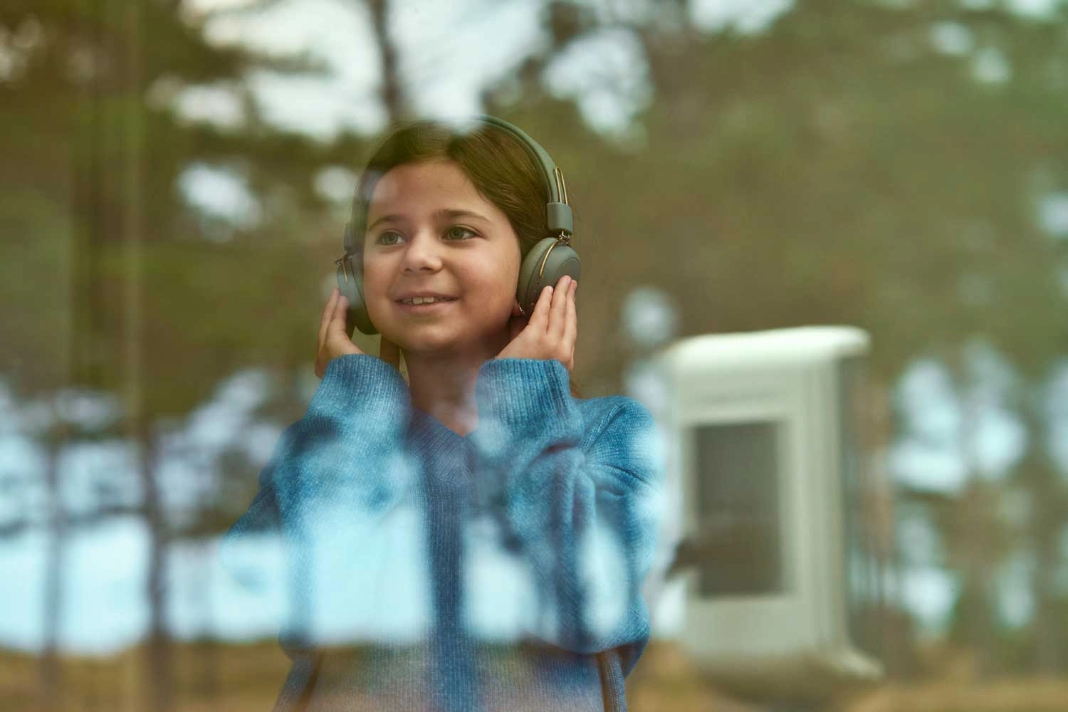 En pige står med hovedtelefoner på og kigger ud ad et vindue