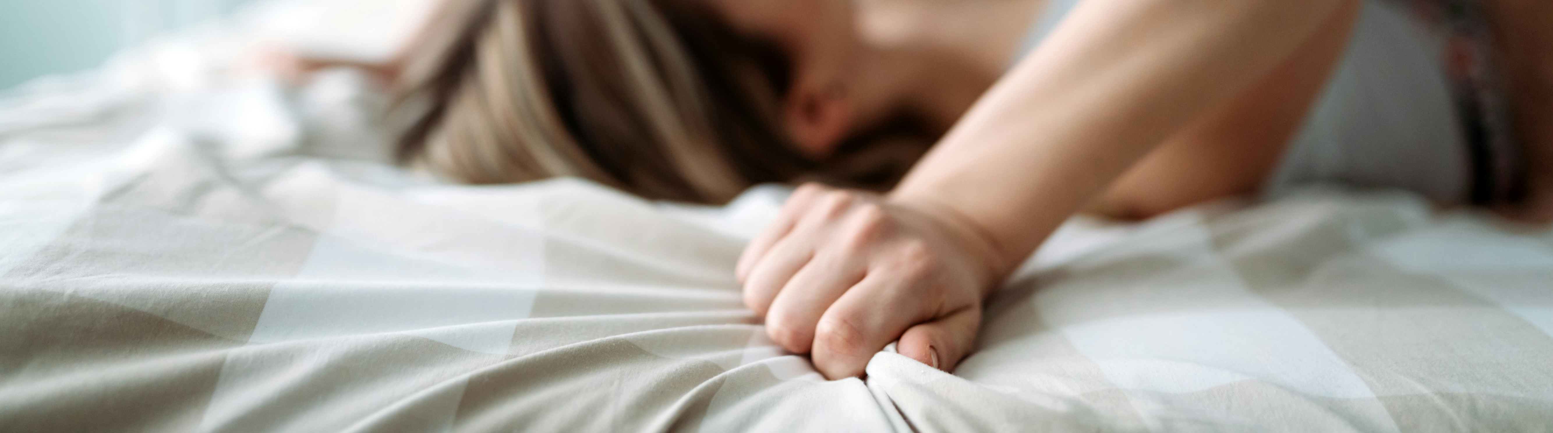 Close-up of a person lying on a bed with one hand gripping the bedsheet in the foreground.