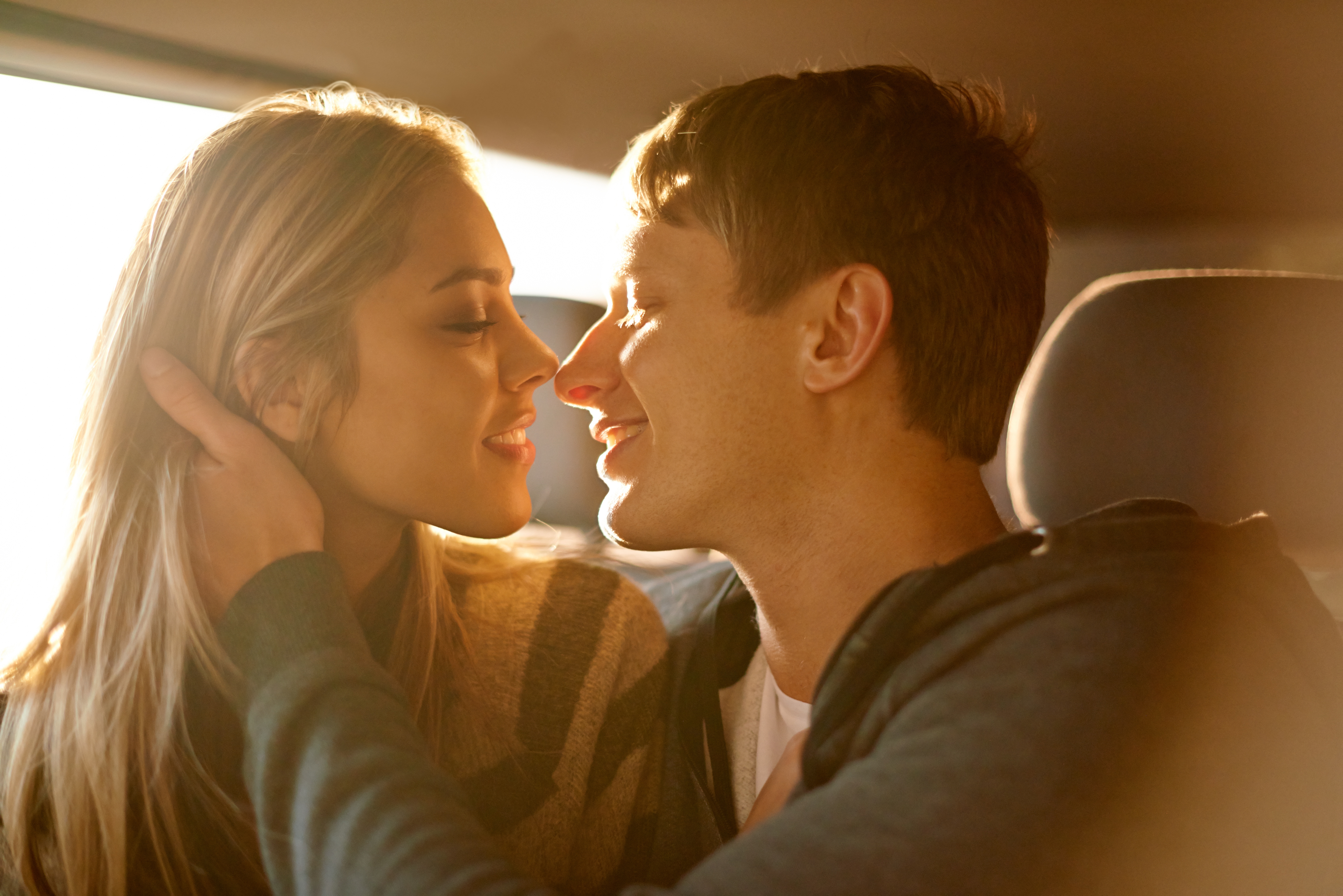 Two adults sitting closely together in a car with their faces nearly touching