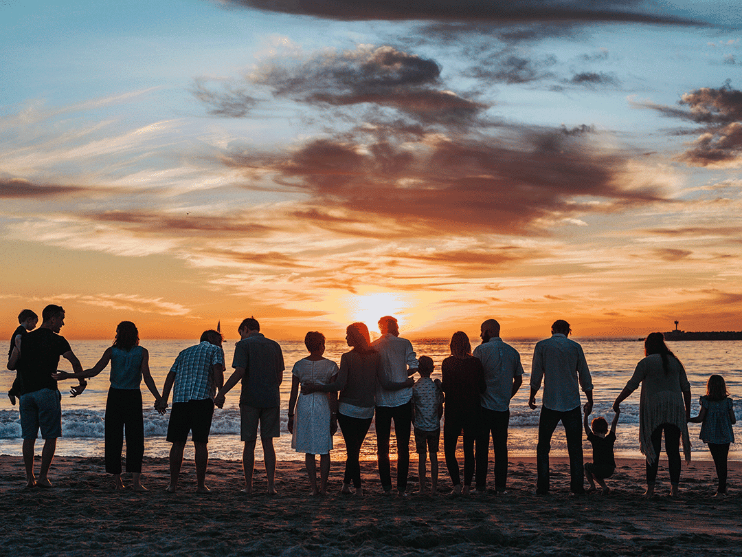 de-de-jwm-ced-cu-hero Eine Gruppe von Menschen, u. a. mit Colitis ulcerosa, genießt den Sonnenuntergang am Meer.