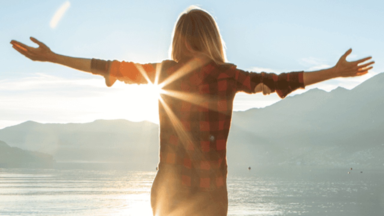 meine_ced_Header_Unterstuetzung_updated Eine einzelne Person ist von hinten zu sehen, steht am Ufer eines Sees mit ausgestreckten Armen. Im Hintergrund Berge, Himmel und tief stehende Sonne mit Lichtstrahlen.