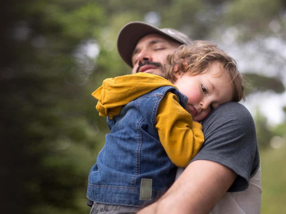 Mann mit Sohn im Arm möchte einen Gentest durchführen lassen Ein Mann mit seinem Sohn im Arm denkt über die Durchführung eines Gentests nach.