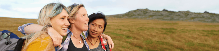 ggd-organisationen-header Zwei Frauen stehen nebeneinander in einer weitläufigen Landschaft und stützen sich gegenseitig.