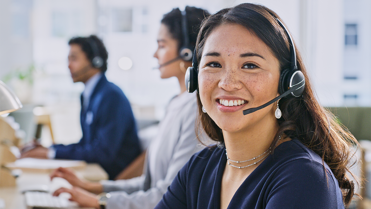 Mehrere Personen sitzen an Schreibtischen in einem modernen Büro und tragen Headsets. Vor ihnen befinden sich Computerbildschirme und Arbeitsmaterialien.