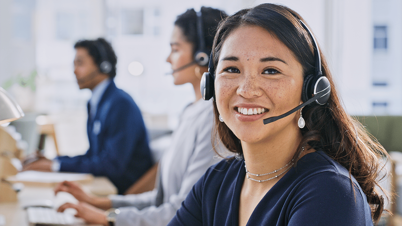 Mehrere Personen sitzen an Schreibtischen in einem modernen Büro und tragen Headsets. Vor ihnen befinden sich Computerbildschirme und Arbeitsmaterialien.