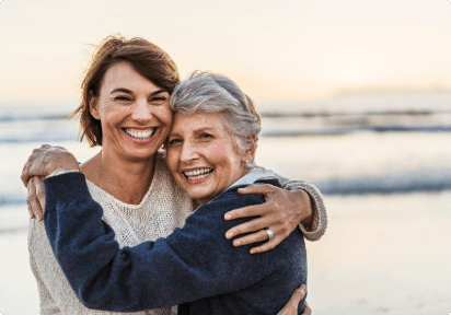 Eine Mutter mit Colitis ulcerosa und ihre Tochter stehen Arm in Arm am Strand. 
