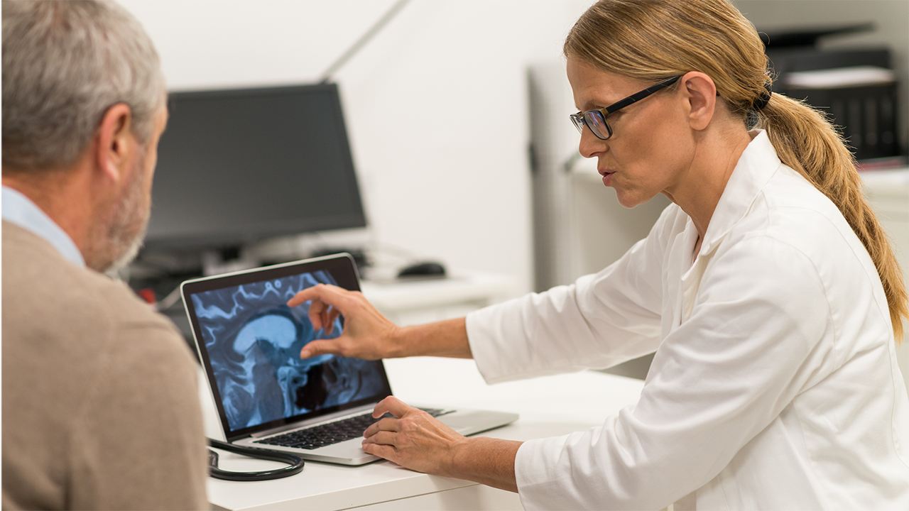 Ärztin erklärt Patienten Gehirnbild auf Laptop-Bildschirm