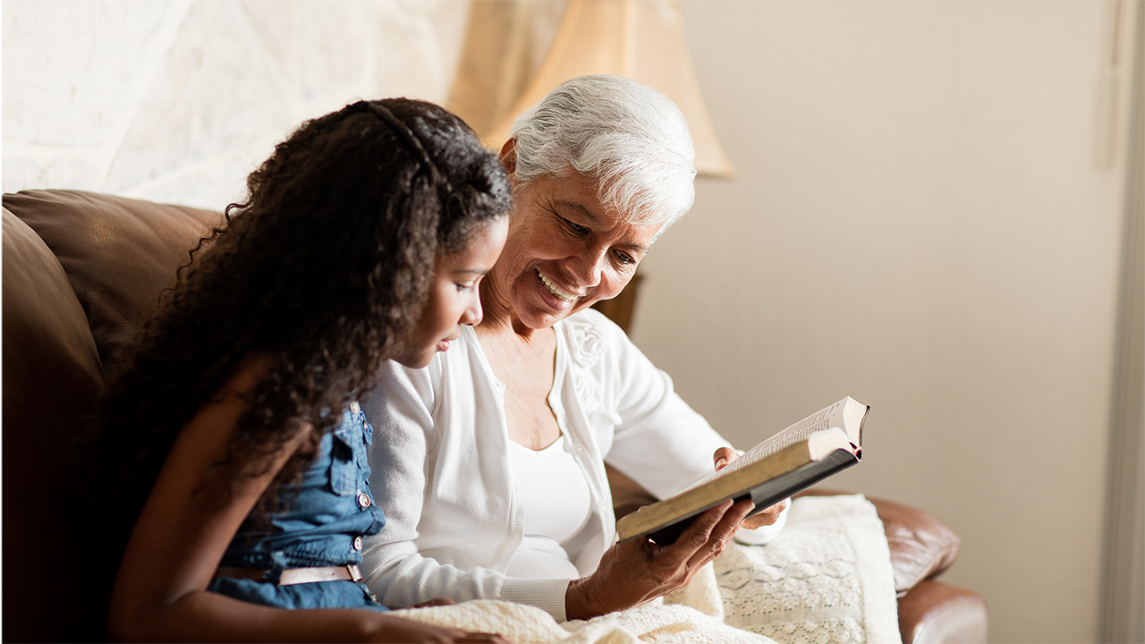 Ältere Frau sitzt mit Kind auf dem Sofa und hält ein Buch