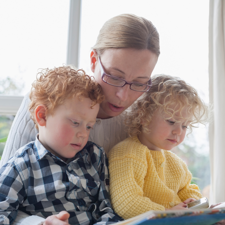 Eine Mutter mit Brille sieht sich gemeinsam mit ihren Kindern ein Buch ein und informiert sich über die Vorteile des Gentests