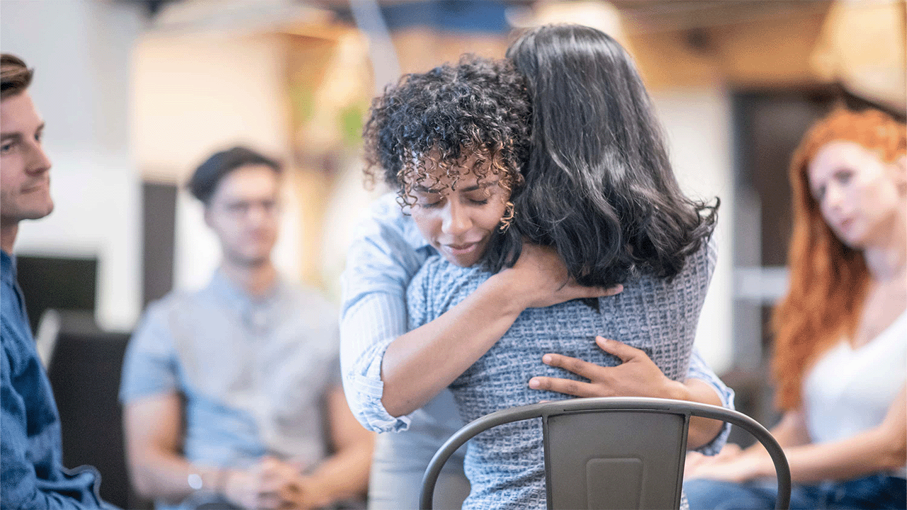 Zwei Frauen nehmen sich in einer Selbsthilfegruppe in den Arm und unterstützen sich emotional.
