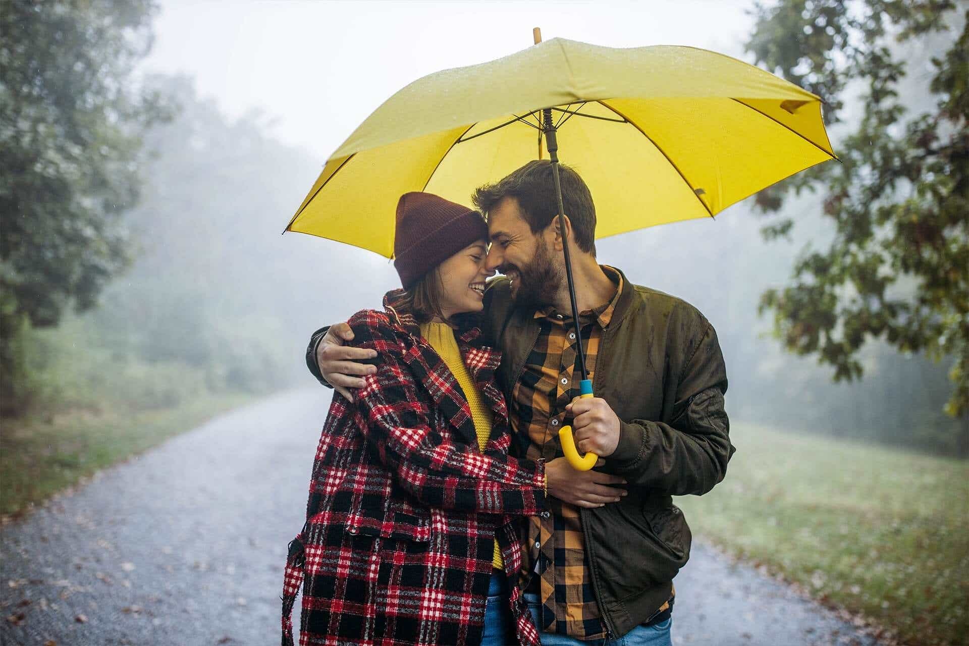 Junges glückliches Paar spaziert im Regen durch den Park
