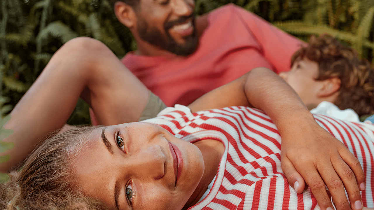 Zu einem gesunden Lebensstil gehört auch ausreichend Entspannung Eine junge Familie liegt entspannt im Gras mit einem Mädchen im Vordergrund.