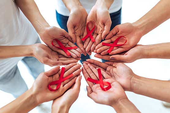 Infektionserkrankungen: Menschen halten die Hände zusammen und präsentieren die HIV-Schleifen #JWM