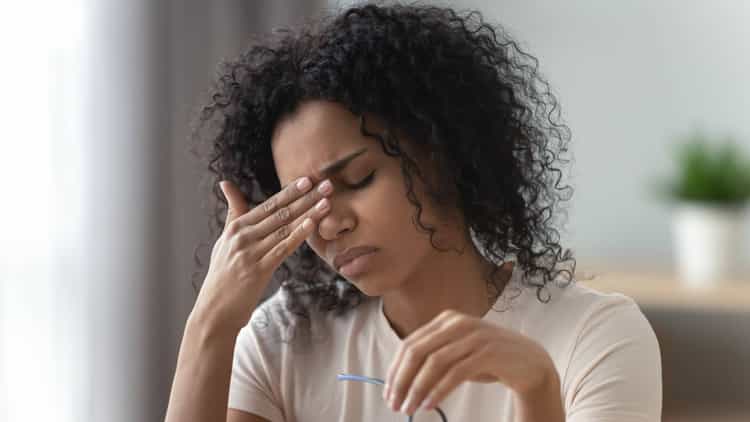 Langanhaltender Stress kann ähnliche Symptome wie Depression auslösen Junge Frau hat die Brille abgenommen und erschöpft die Augen geschlossen, während sie ihre Stirn auf die Hand stützt.