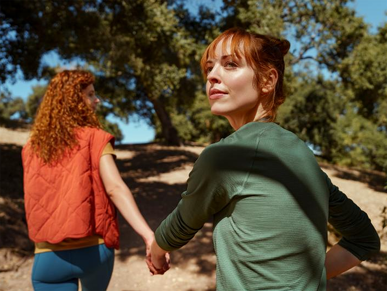 Zwei erwachsene Frauen laufen, sich an der Hand haltend, durch den Wald