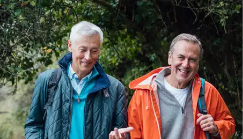 Zwei ältere Männer in Outdoorkleidung beim Wandern im Wald.