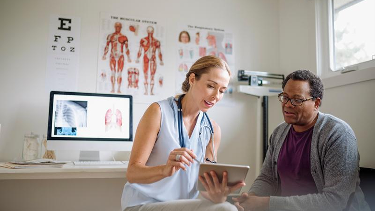 Ärztin erklärt ihrem Patienten etwas auf einem Tablet