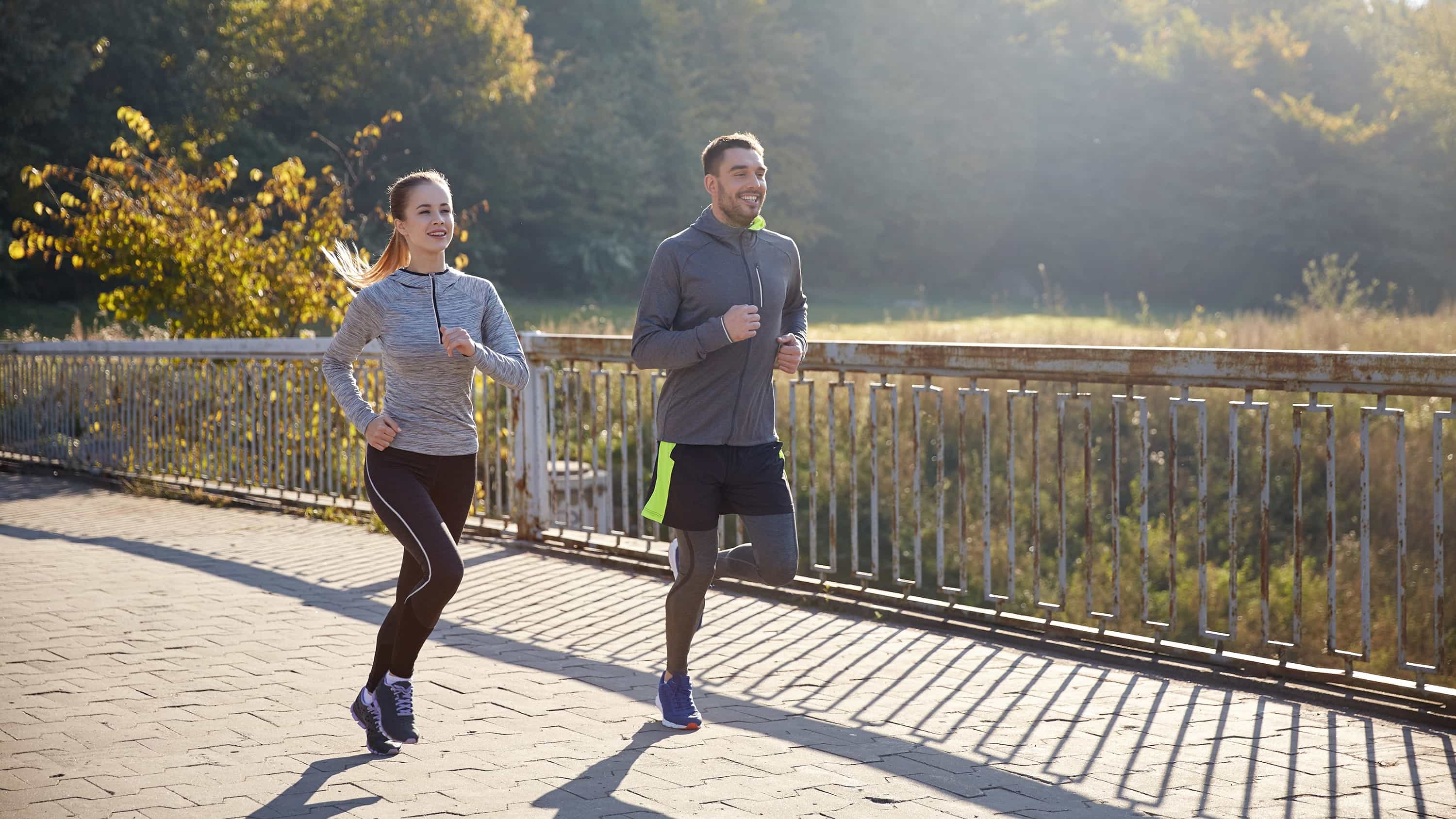 Eine Frau und ein Mann joggen durch eine spätsommerliche Landschaft. Ausdauertraining hilft bei Depression.
